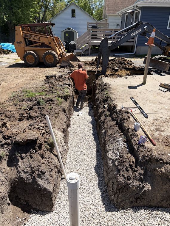 Long open utility trench with crew and skid steer running a new sewer line