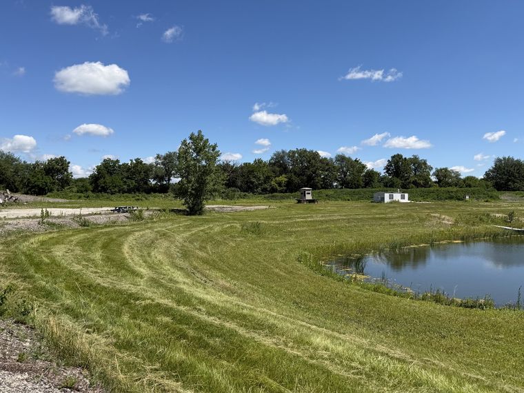 Wide mowed field with cut stripes curving around a farm pond