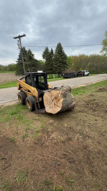 Skid steer carrying a large landscape boulder across a lawn