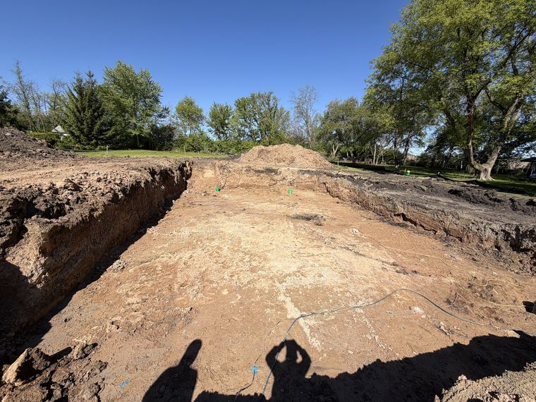 Large open foundation excavation cut into a wooded residential lot