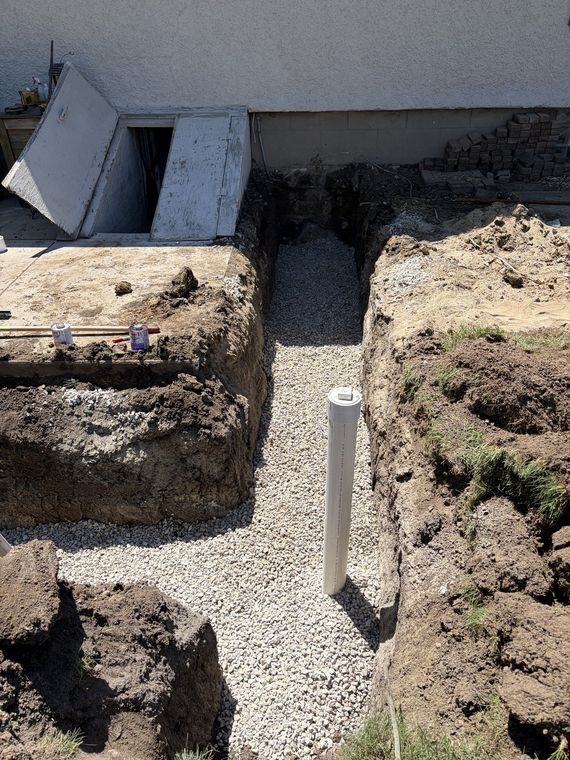 Sewer trench with a white cleanout riser set in washed stone