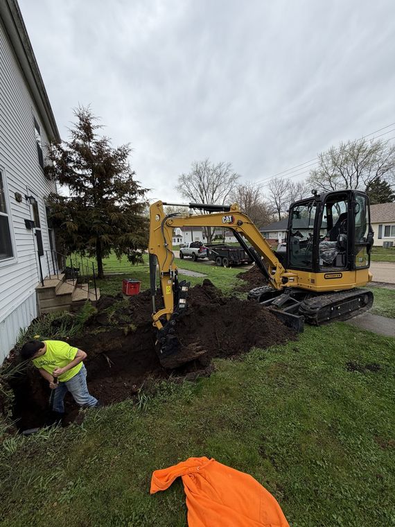 Mini excavator and a worker in high-visibility clothing digging a trench beside a house