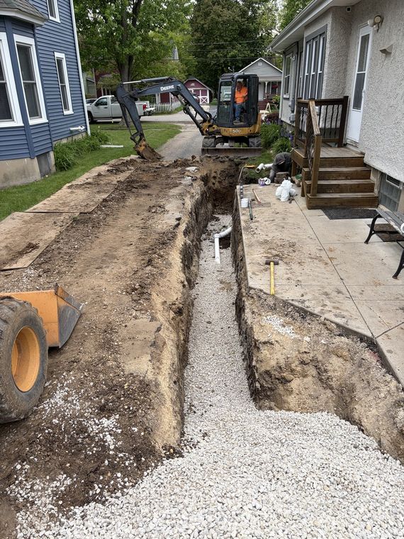 Open trench and stone bedding running alongside a house to the street