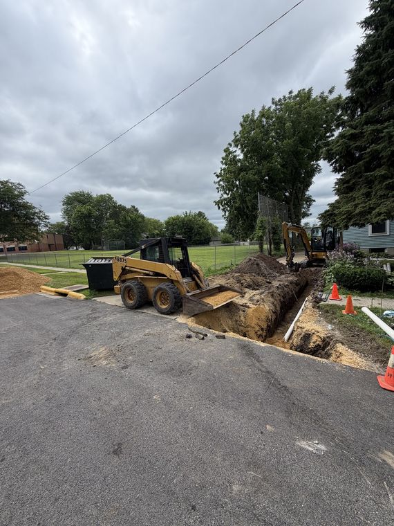 Skid steer and open trench cut across a residential driveway