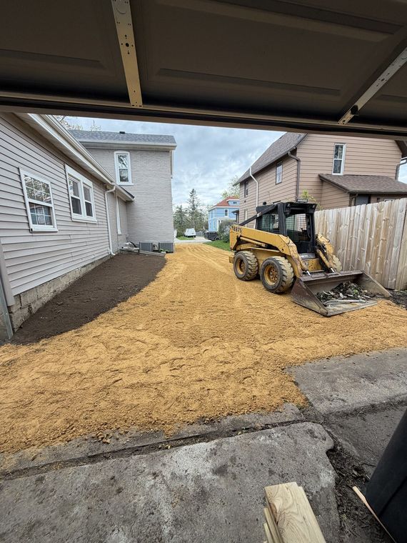 Skid steer spreading fresh gravel in a narrow side yard between two houses