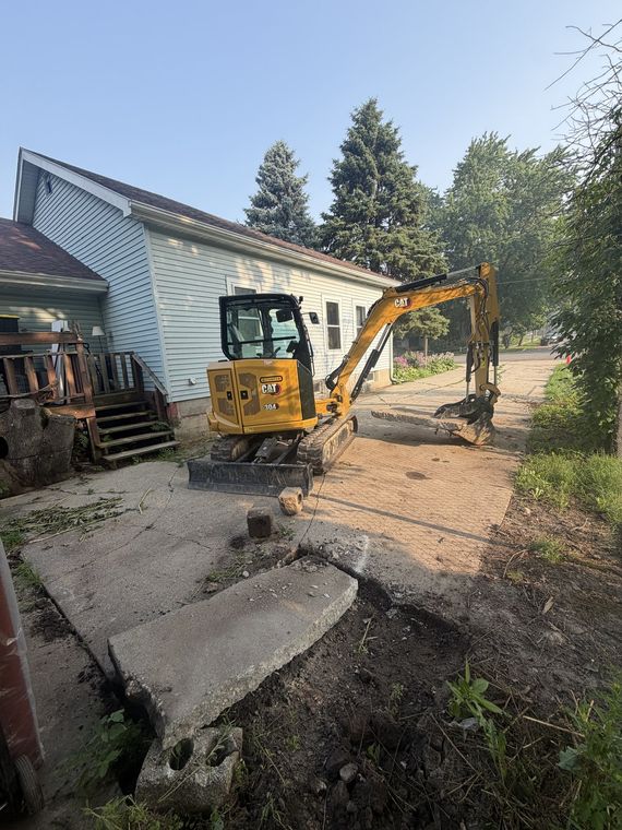 Excavator removing broken concrete slabs beside a house