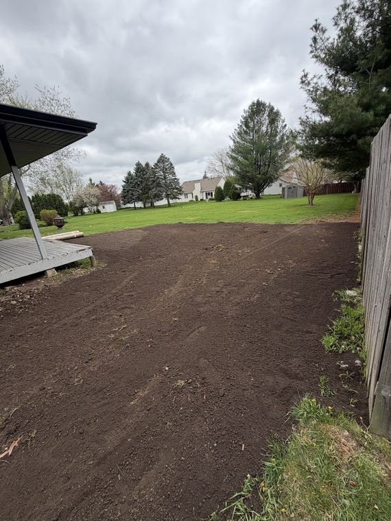 Backyard graded down to bare soil between a house and a wooden fence