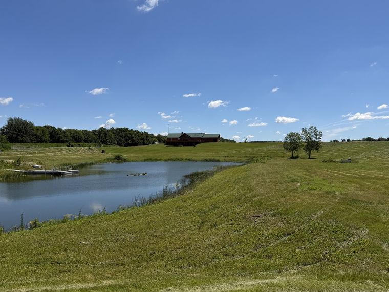 Freshly mowed acreage sloping down to a farm pond on a clear day